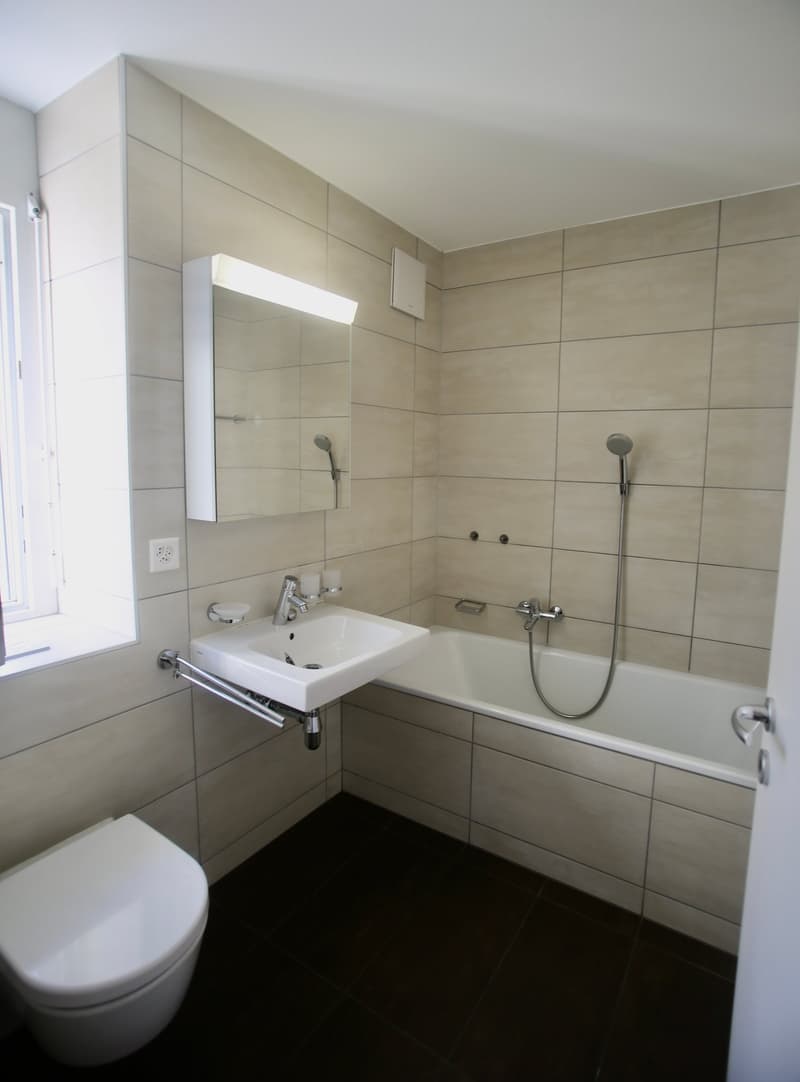 tiled floor, white bathtub, wall-mounted sink, mirror, toilet, showerhead, faucet