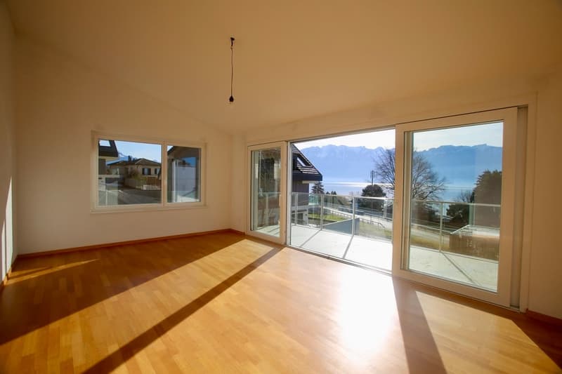 Empty room with large sliding glass doors leading to a balcony and a lake view