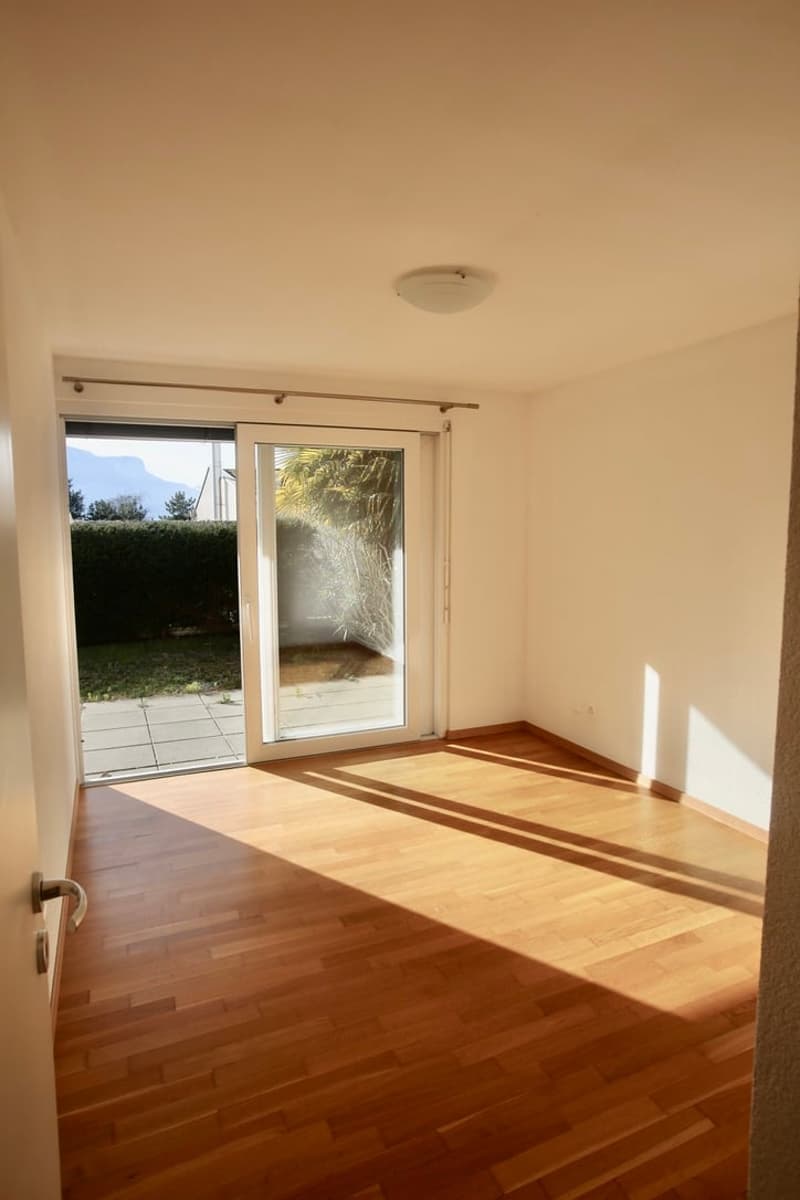 Open room with wooden floors, sliding doors leading to balcony, white walls, ceiling lamp