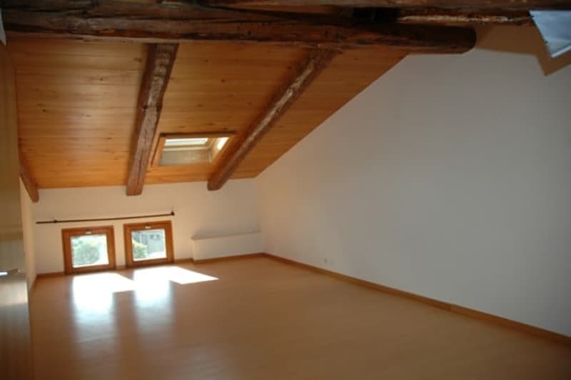 Empty room with wooden floor, wooden ceiling, two windows, and white walls.
