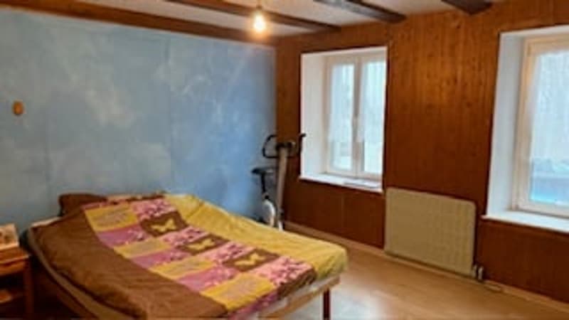 bed with multi-colored quilt, wooden floor, wooden wall, exercise bike, radiator, window