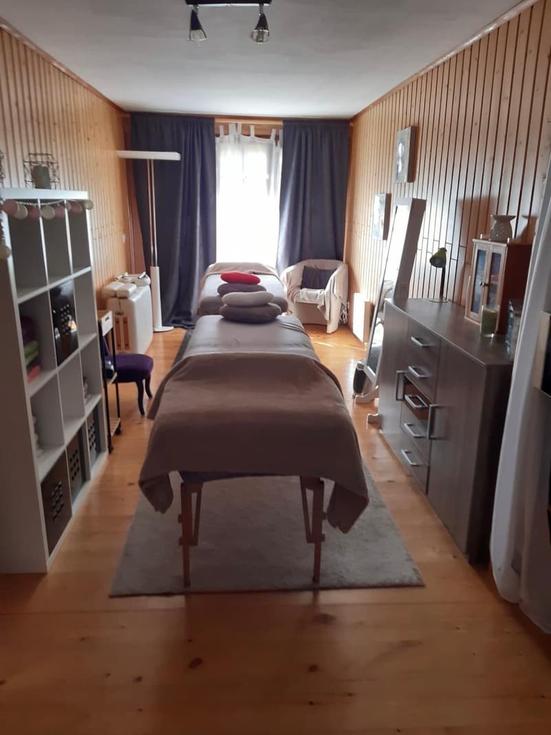 room with two massage tables, wooden flooring, wooden paneling, shelves, chair, lamp, and window with white curtains