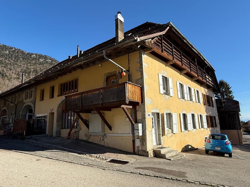 3 story house, yellow exterior, wooden balcony, multiple windows, chimney, blue car parked in front
