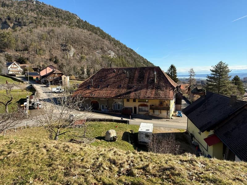 A large yellow house with brown roof, situated in the village at the foot of the mountain with several other houses