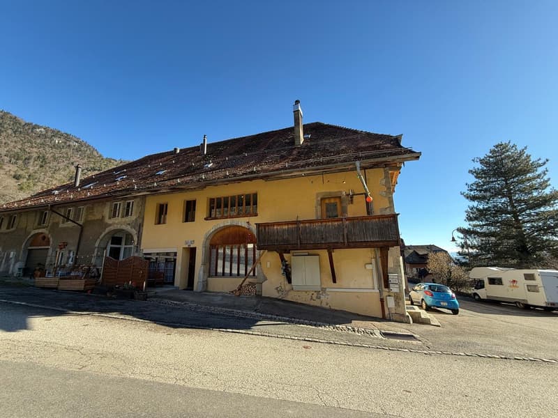 Yellow building with brown roof, wooden balcony, multiple windows, located at the base of a mountain