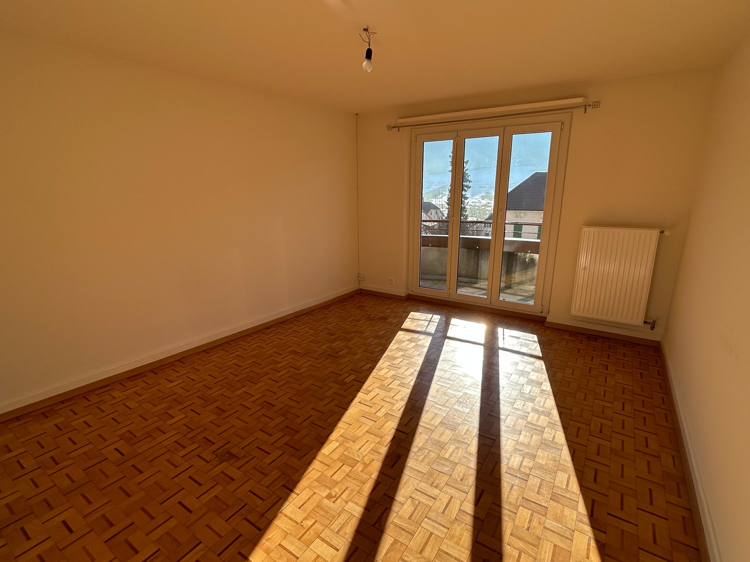 Empty room, parquet floor, white walls, sliding glass door to a balcony