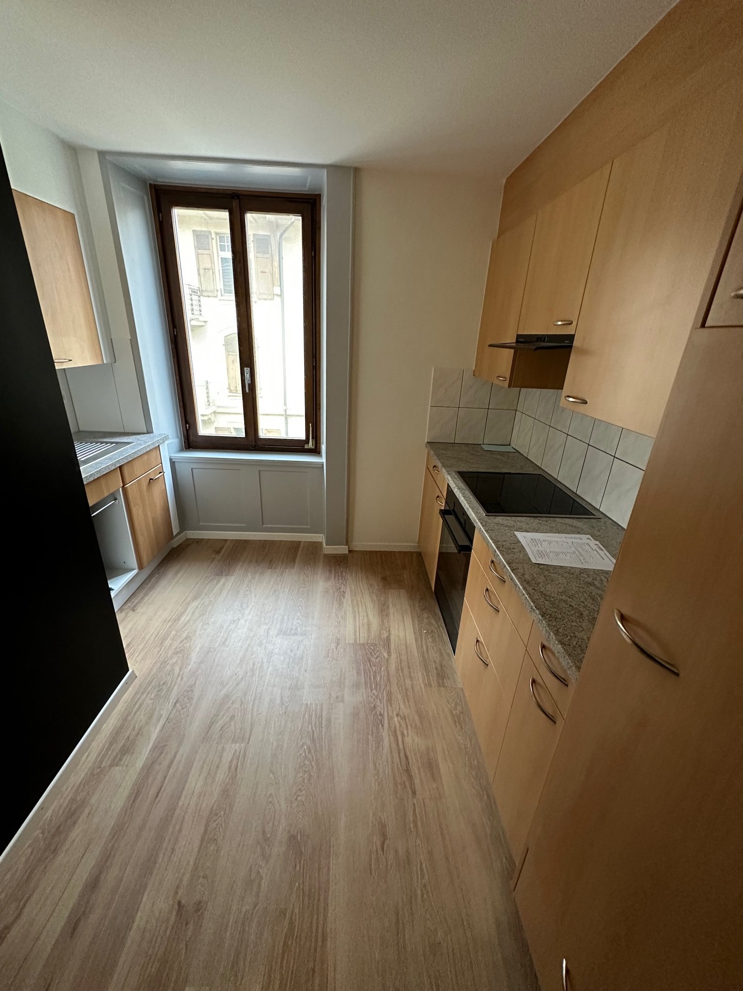 Modern kitchen with wooden flooring, countertops, gas stove, oven, cabinets, sink, and window.