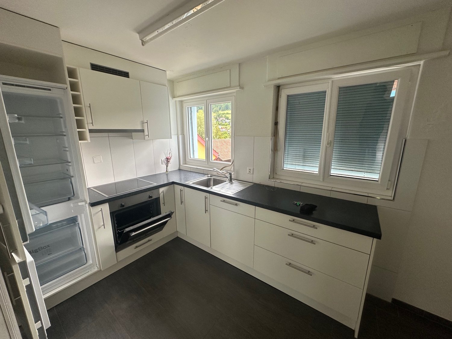 modern kitchen with white cabinets, black countertops, stainless steel appliances, double sink, and a window with blinds
