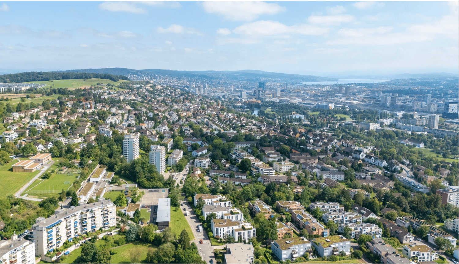 City skyline with residential and commercial buildings, green spaces, and surrounding landscapes