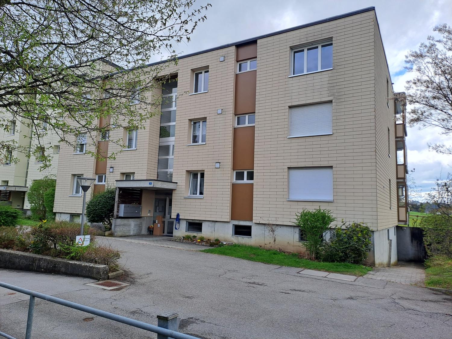 5 story building, brown brick, multiple windows, entrance with ramp, parking lot in front