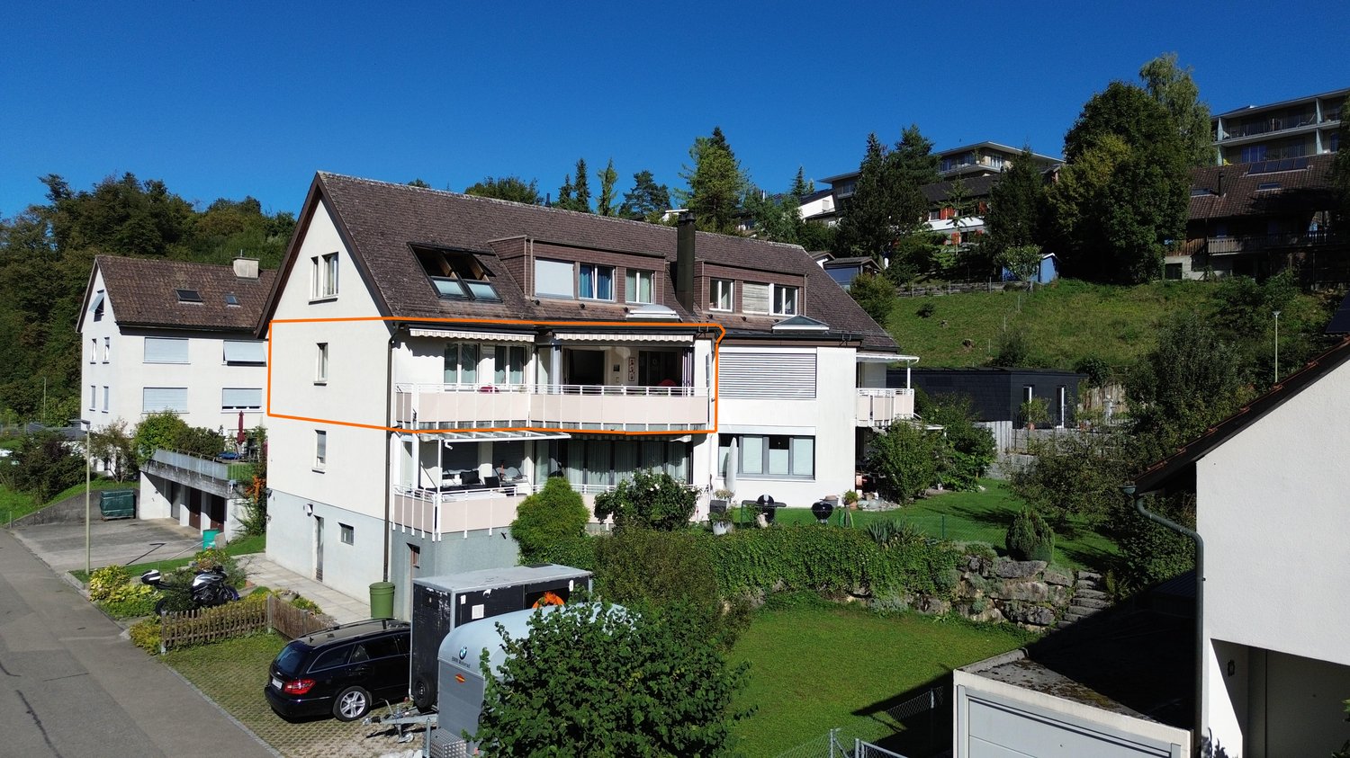 2 story house, brown roof, white walls, two balconies, a garden, and a car parked outside.