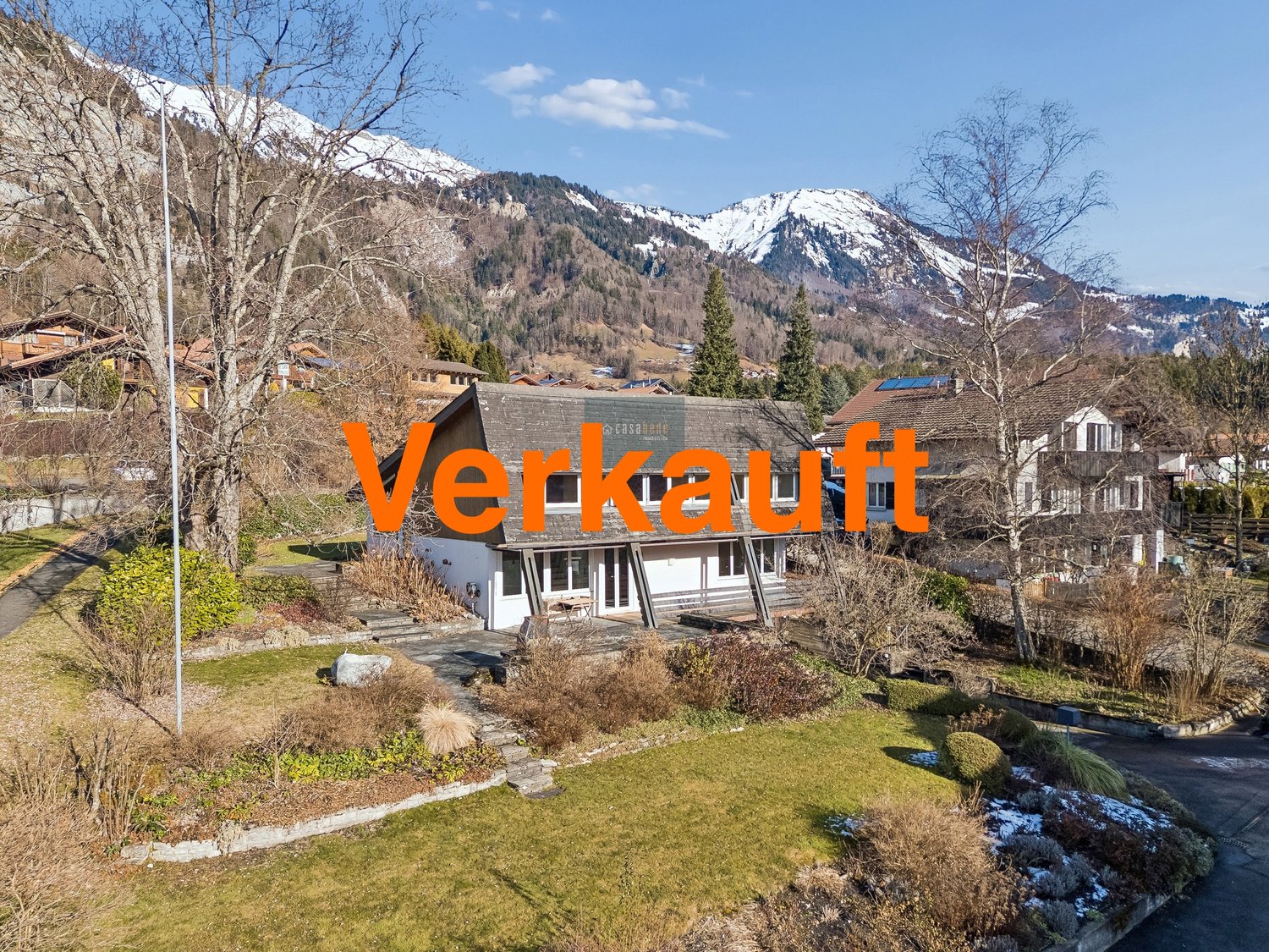 Detached house, white exterior, gray roof, surrounded by trees, mountains in the background, driveway