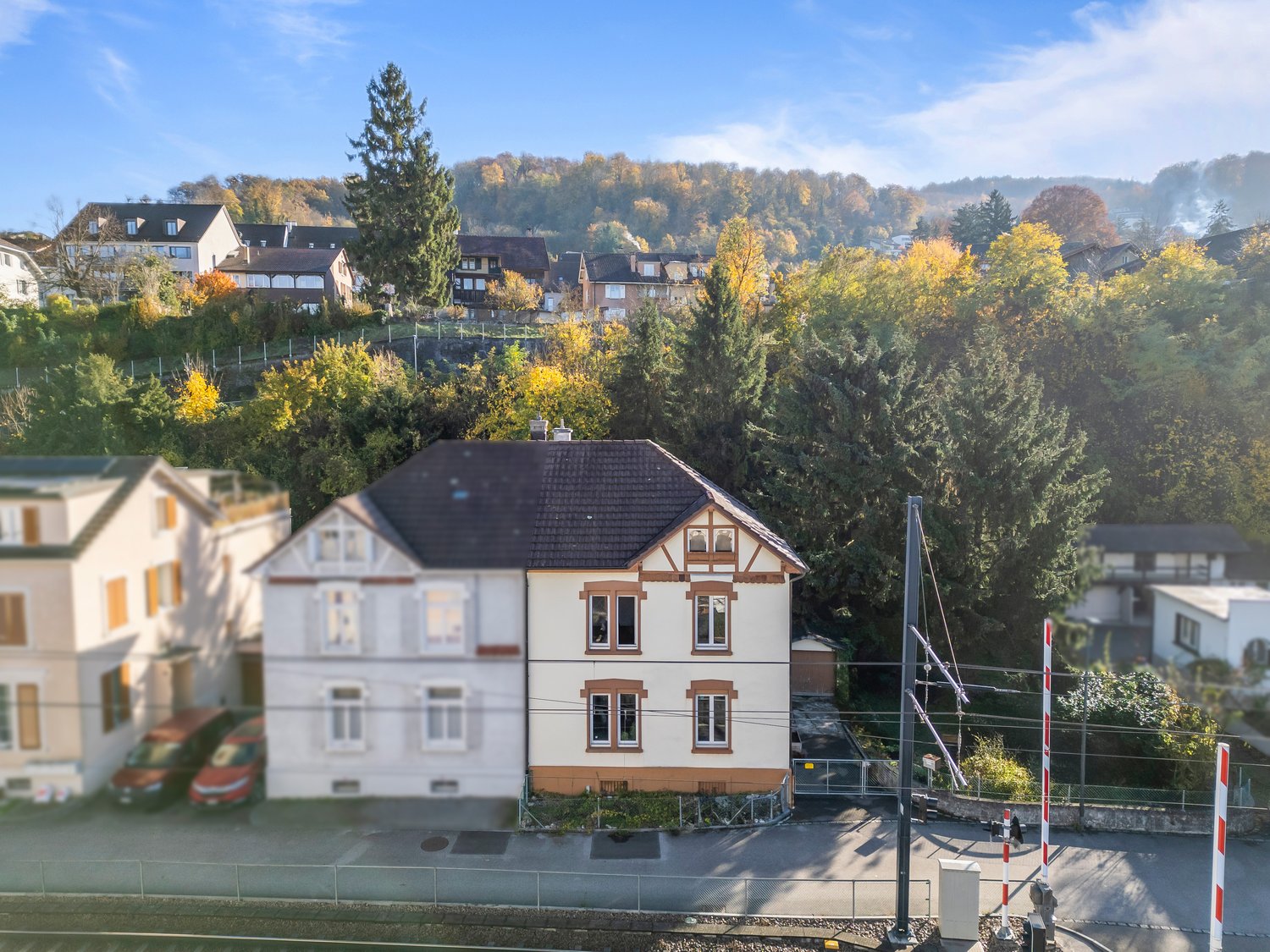 Single family house on hill, surrounded by other houses and trees, one car parked