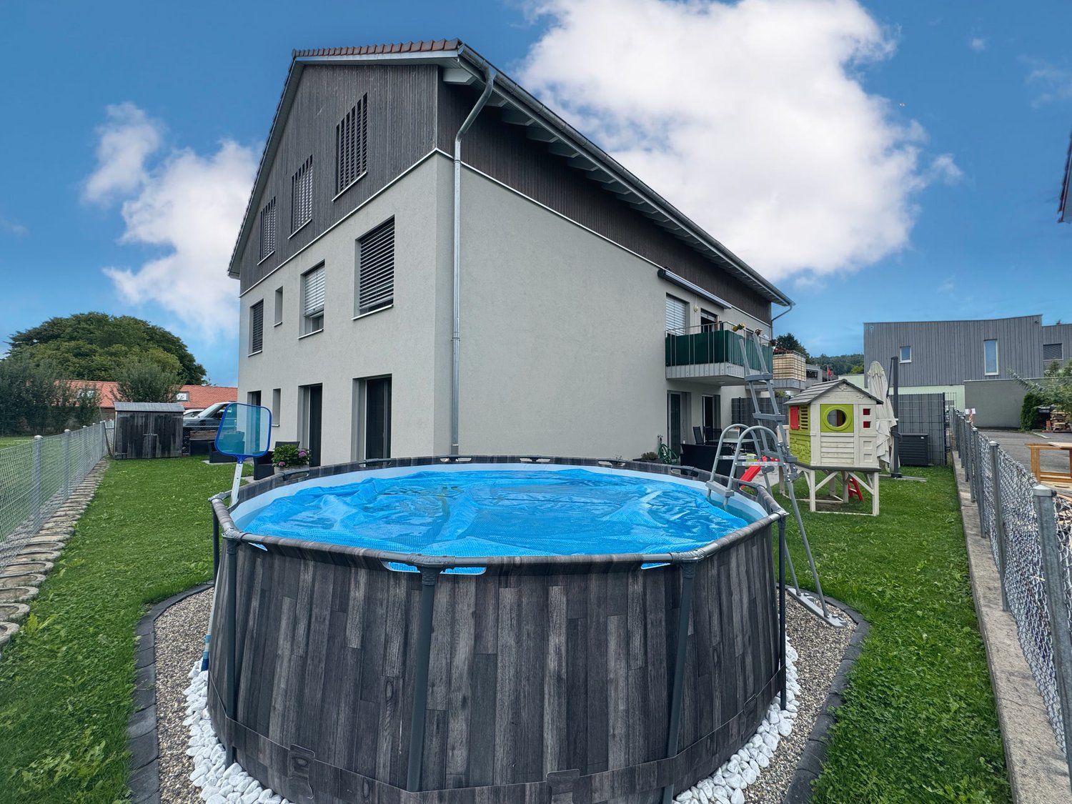 Modern house with pool, fenced yard, balcony with railings, covered playground, surrounding trees