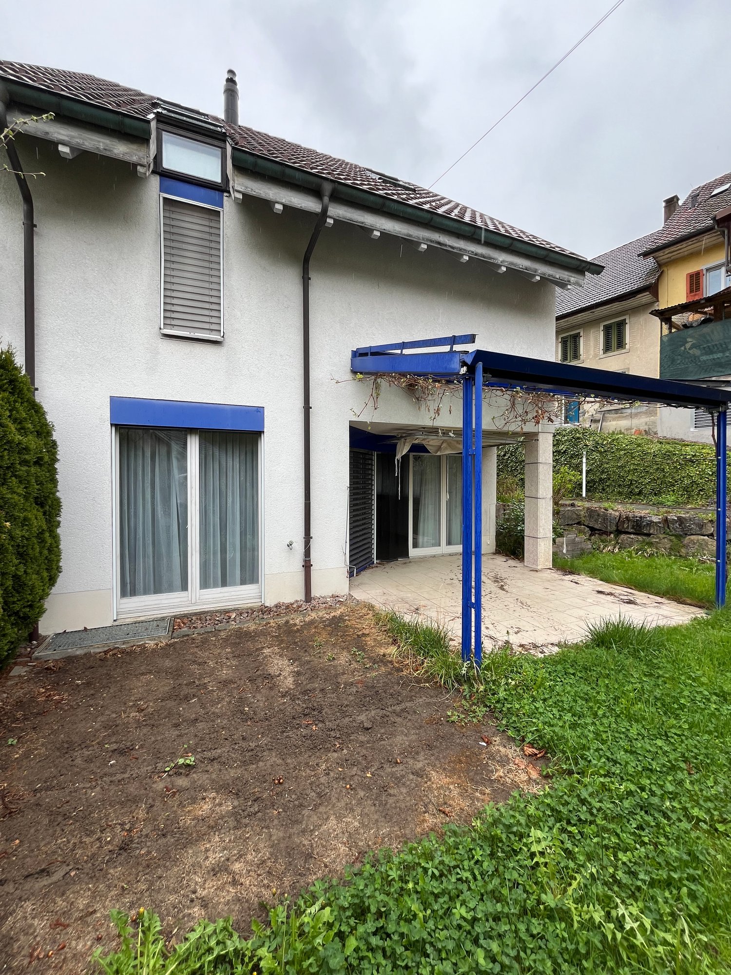 white house, brown tiled roof, blue awning, open garage with paved floor