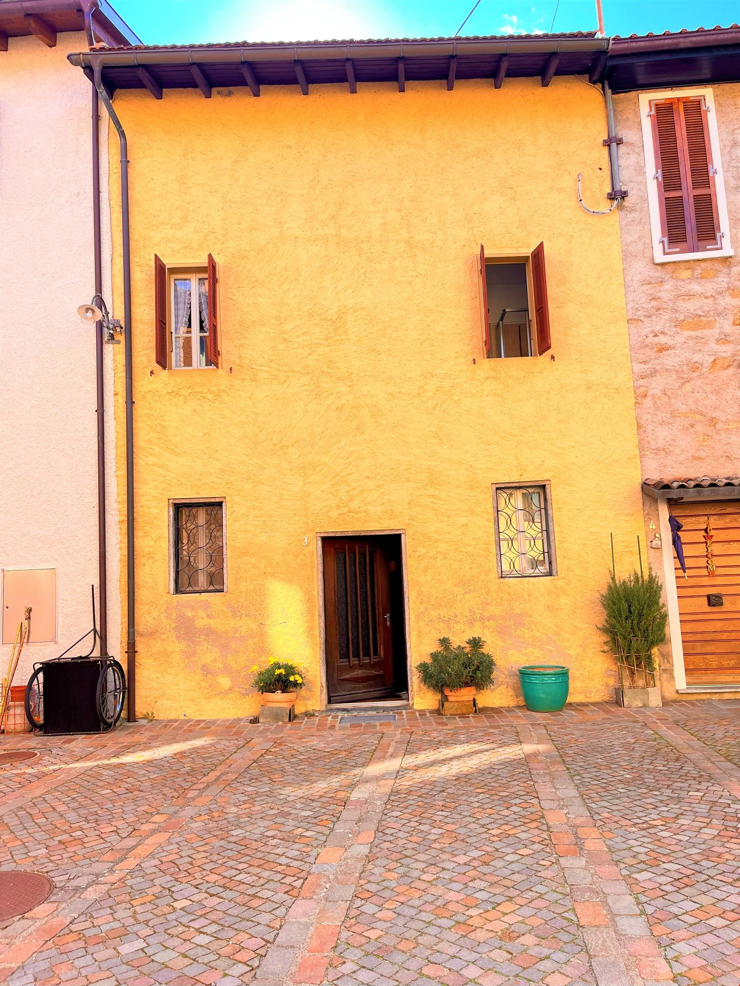 yellow brick building, wooden door, three windows, brick paved courtyard, plants