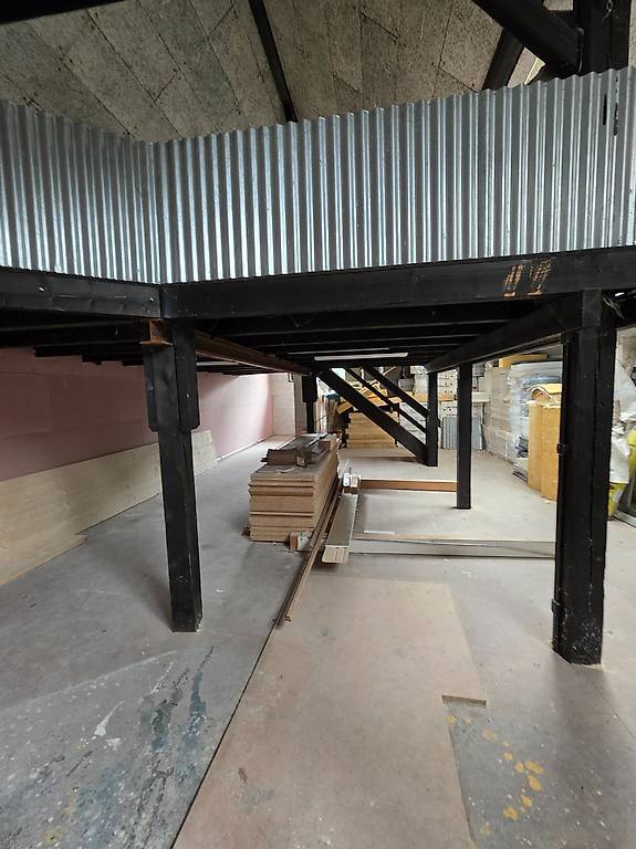 interior of a building, raised ground floor, corrugated metal roof, metal support beams, concrete floor, stack of wooden planks