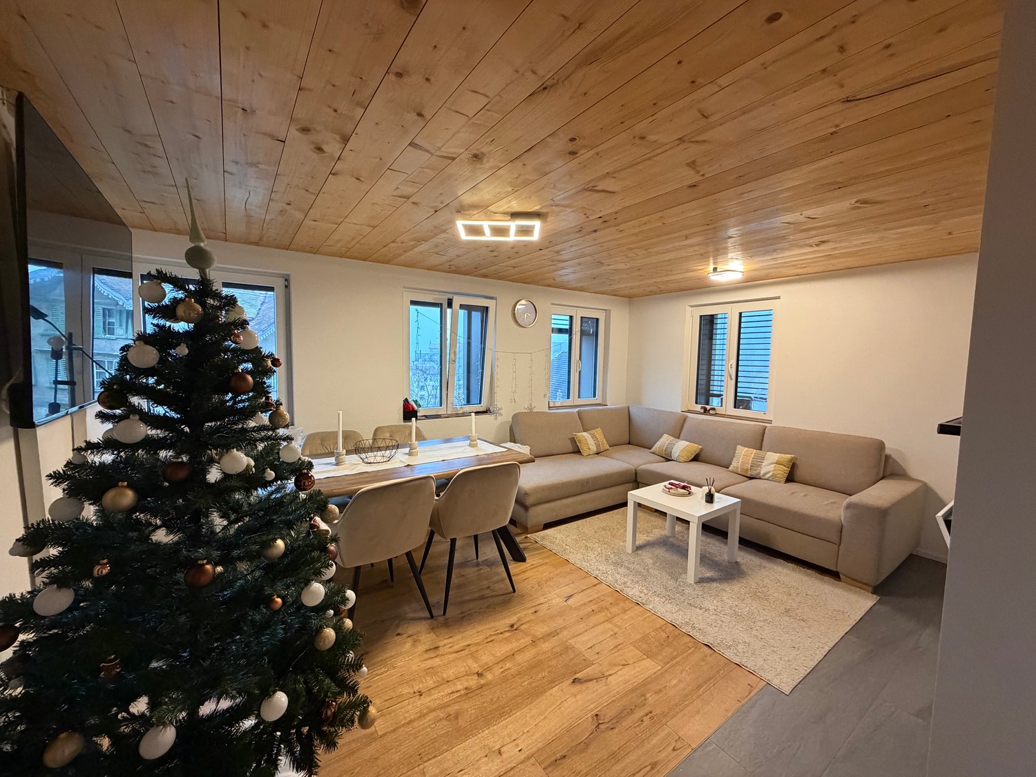 Living room with wooden floor, Christmas tree, sofa, table, carpet, dining chairs, coffee table, clock