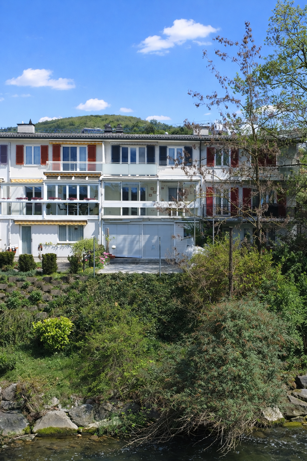 3 story apartment building, white exterior, red shutters, balconies, garage, garden, river view