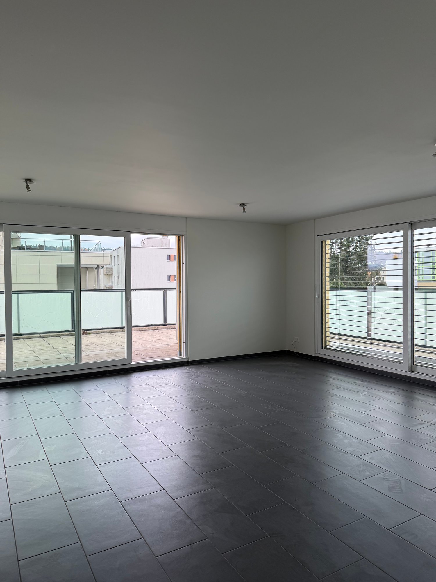 Empty room with sliding glass doors leading to a balcony, glass window with blinds, ceiling mounted lights