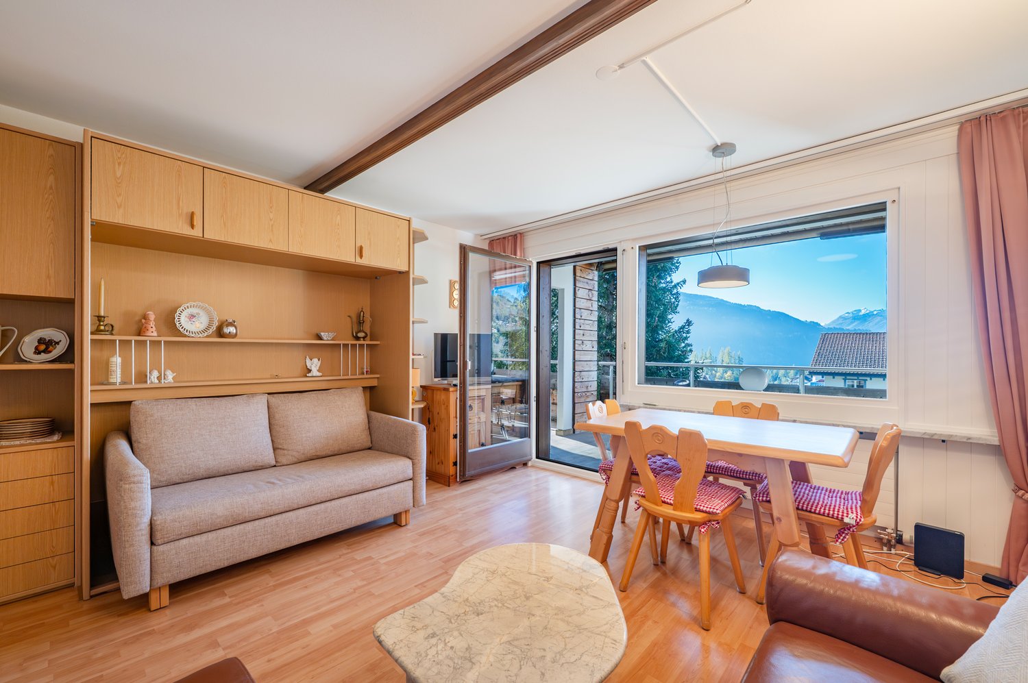 wooden floor, couch, tv cabinet, dining table with chairs, shelf with items, balcony access