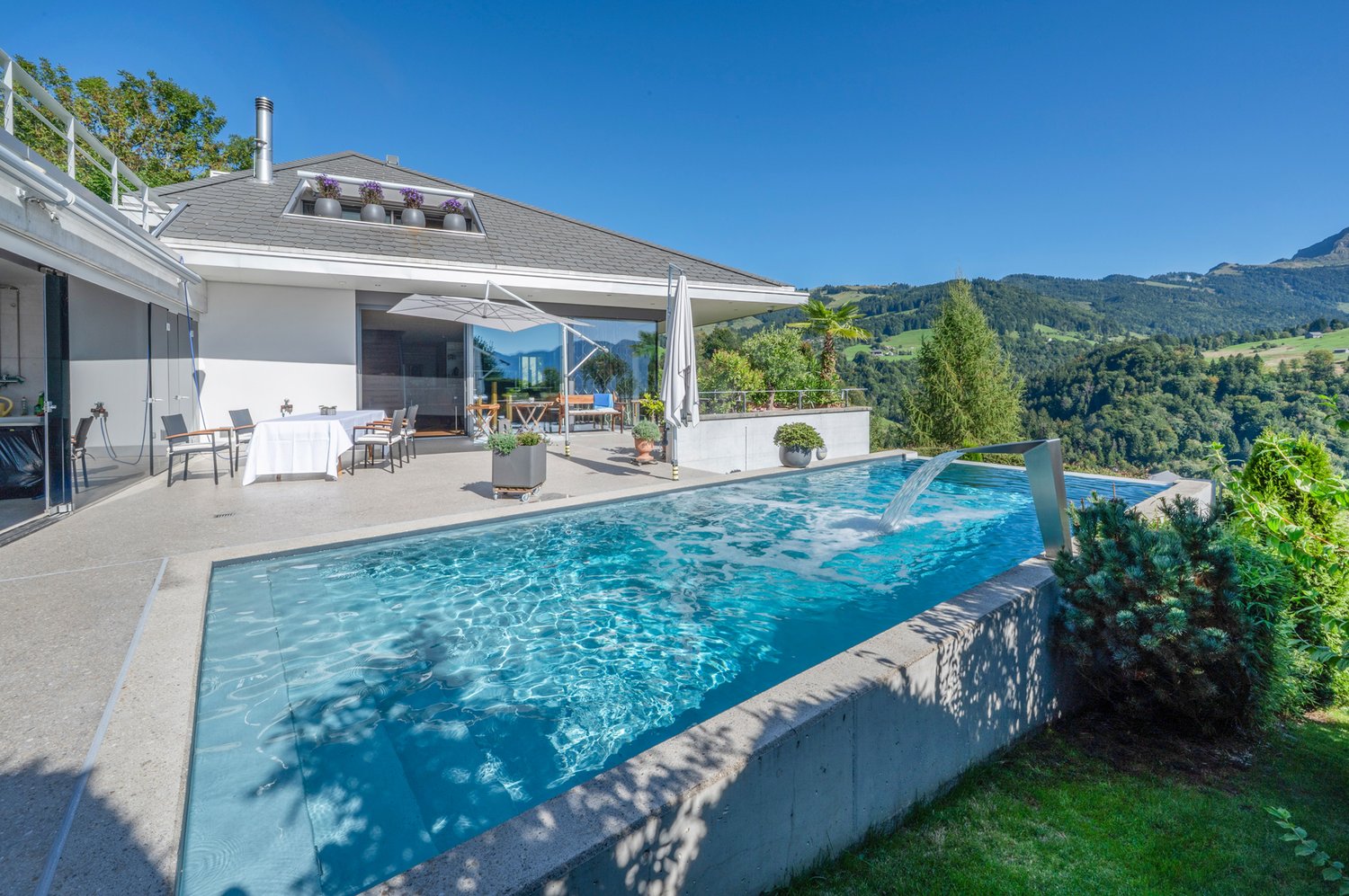 swimming pool, garden, grassy area, dining area with table and chairs, house with glass door and balcony