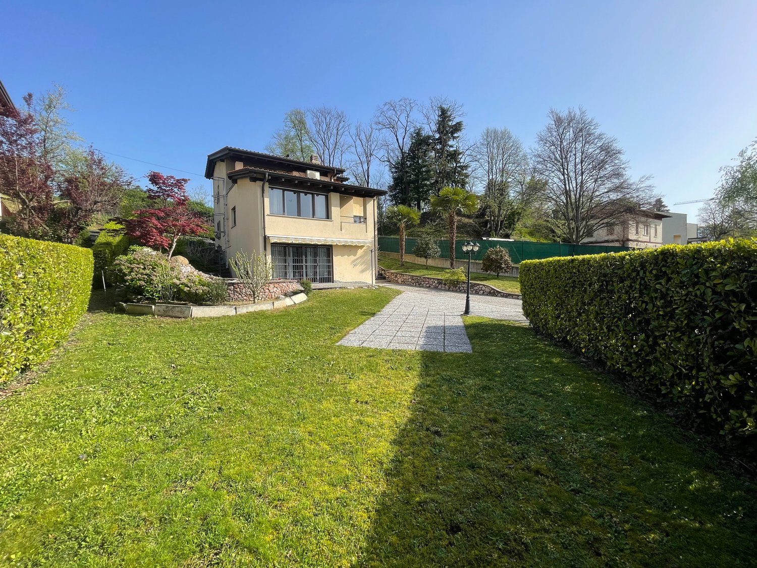 Two-story house with a garden, pathway leading to the front entrance, hedges, and a large grassy lawn