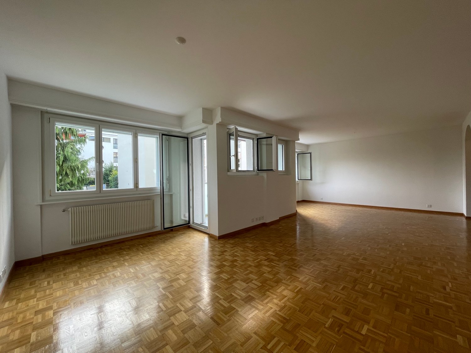 open room with windows, white walls, wooden floors, radiator, sliding glass doors