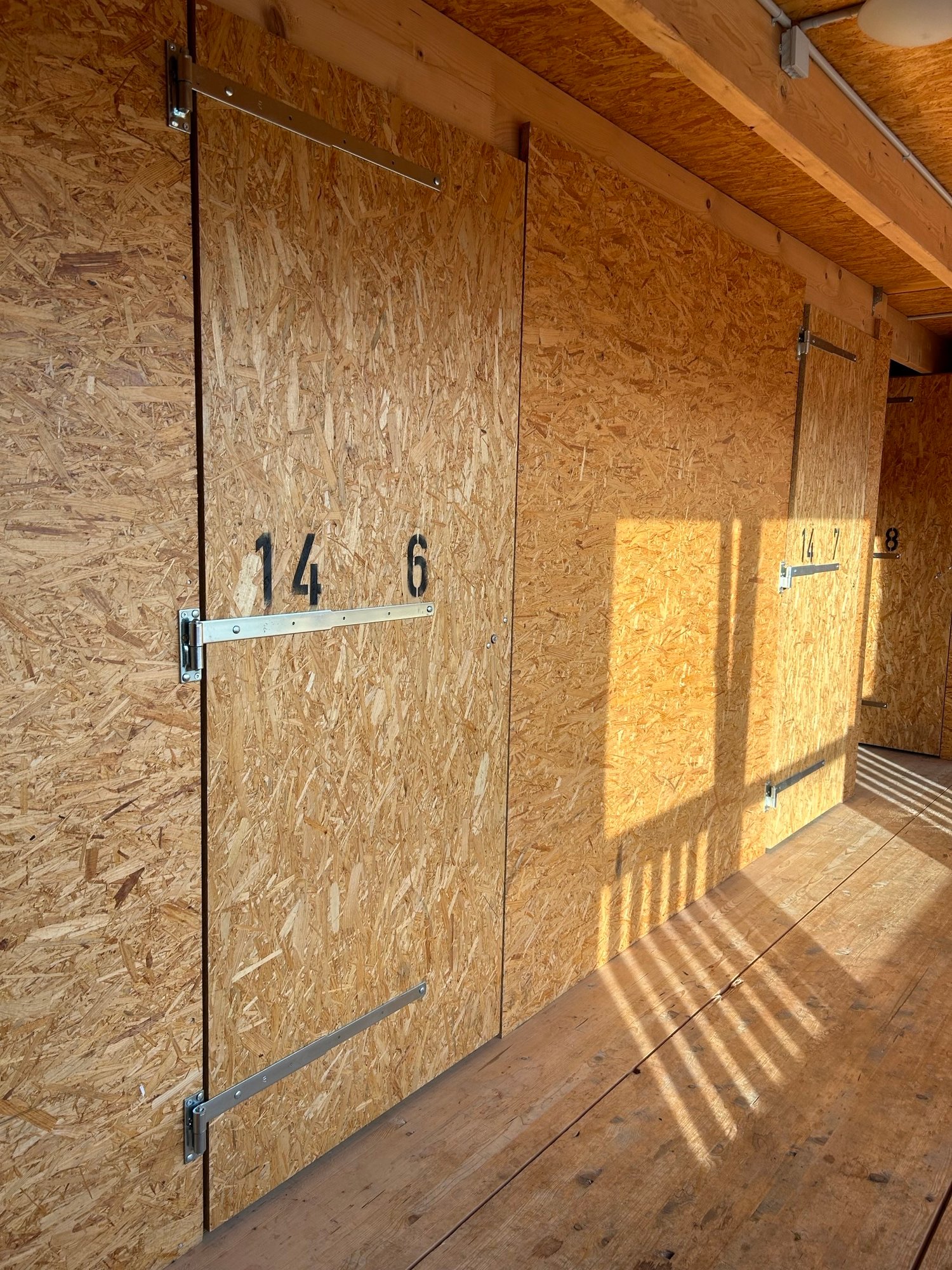 Interior of a storage shed with wooden floor, metal doors, and particleboard walls.