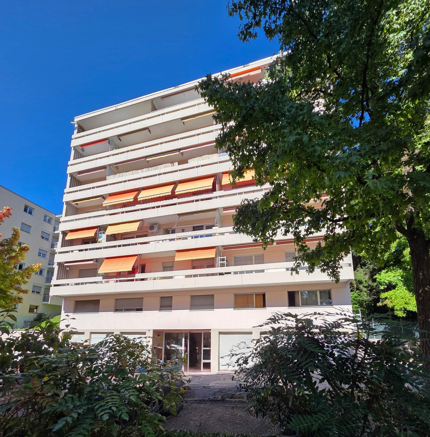 White multi-story building, several balconies with awnings, windows, multiple air conditioners