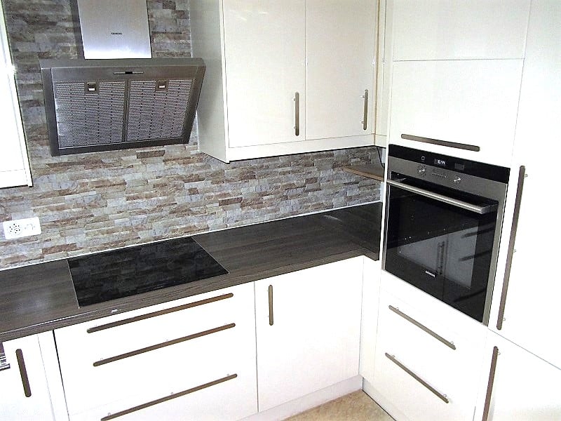Modern kitchen with white cabinets, black countertops, stone backsplash, built-in oven and dishwasher