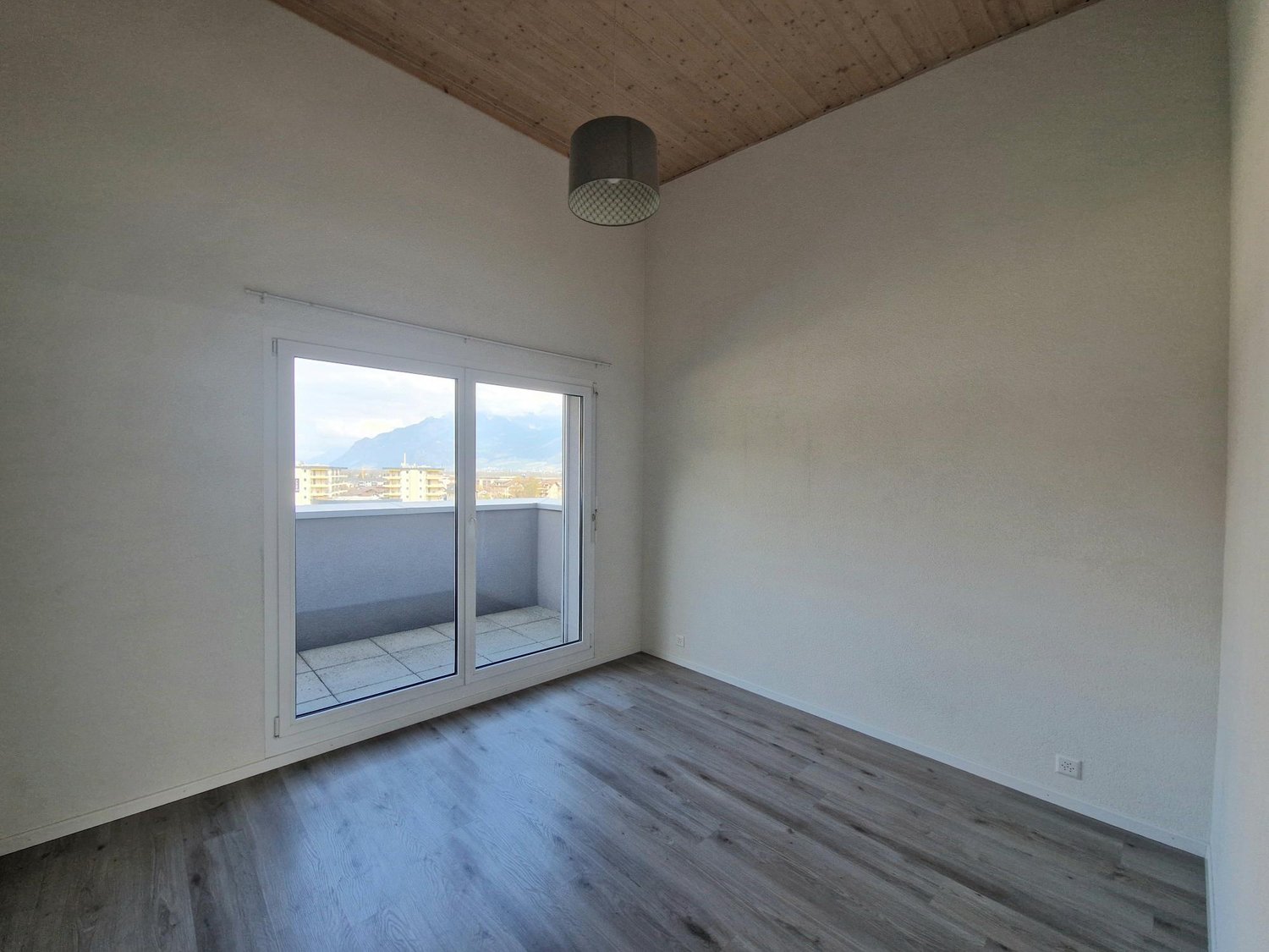 Spacious bedroom with large windows, hardwood-style flooring, and a balcony or terrace overlooking the surrounding area.