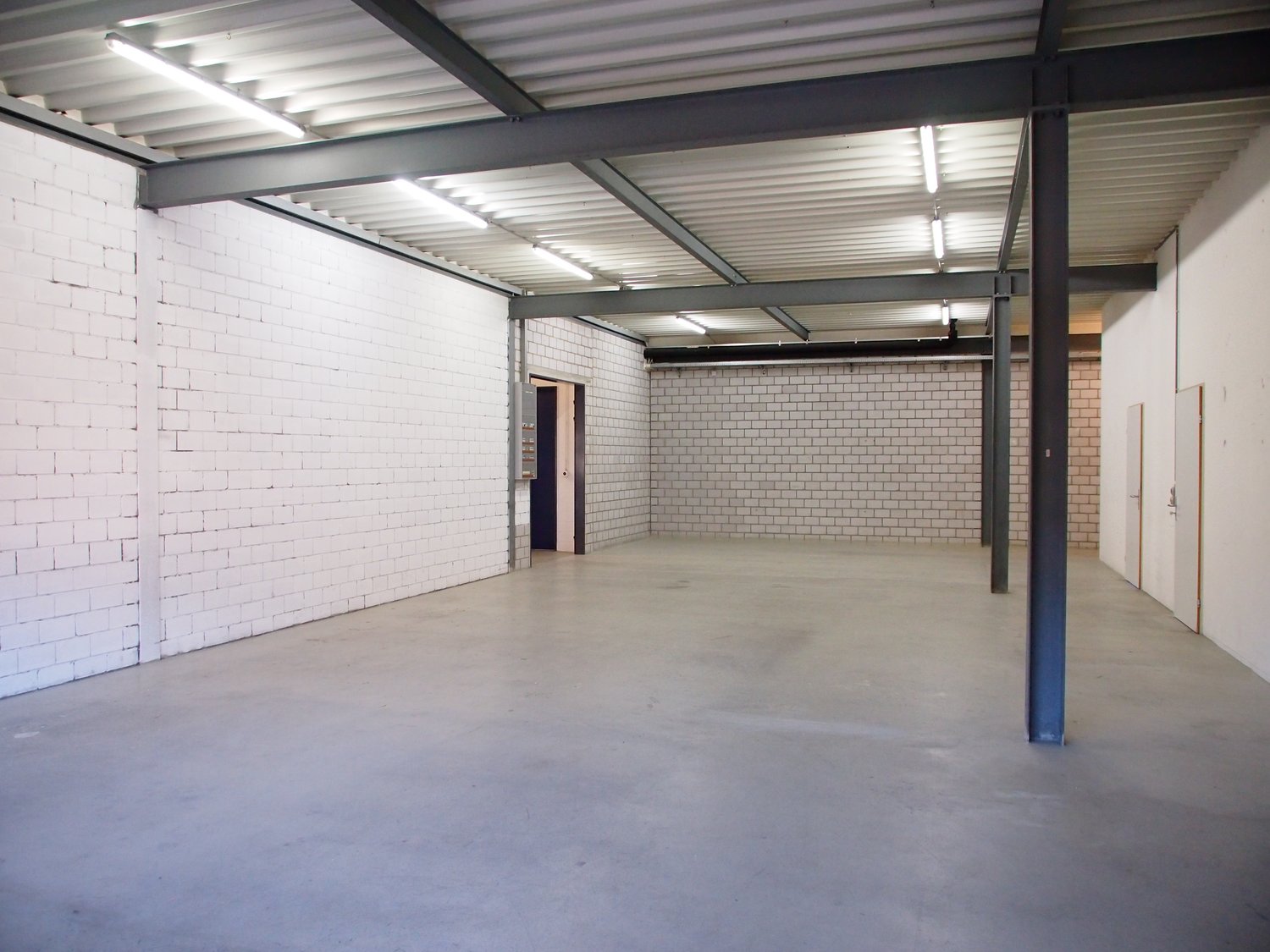 empty industrial warehouse with brick walls, concrete floor, metal beams, fluorescent lights