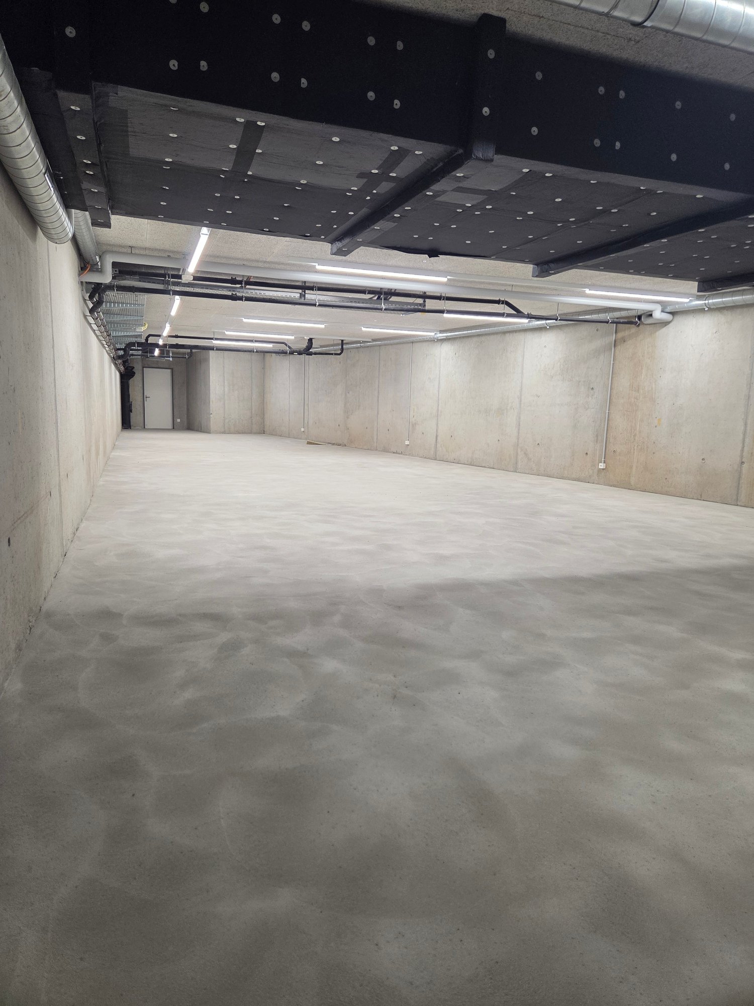 Empty concrete floor, metal beams, pipes, lights, door