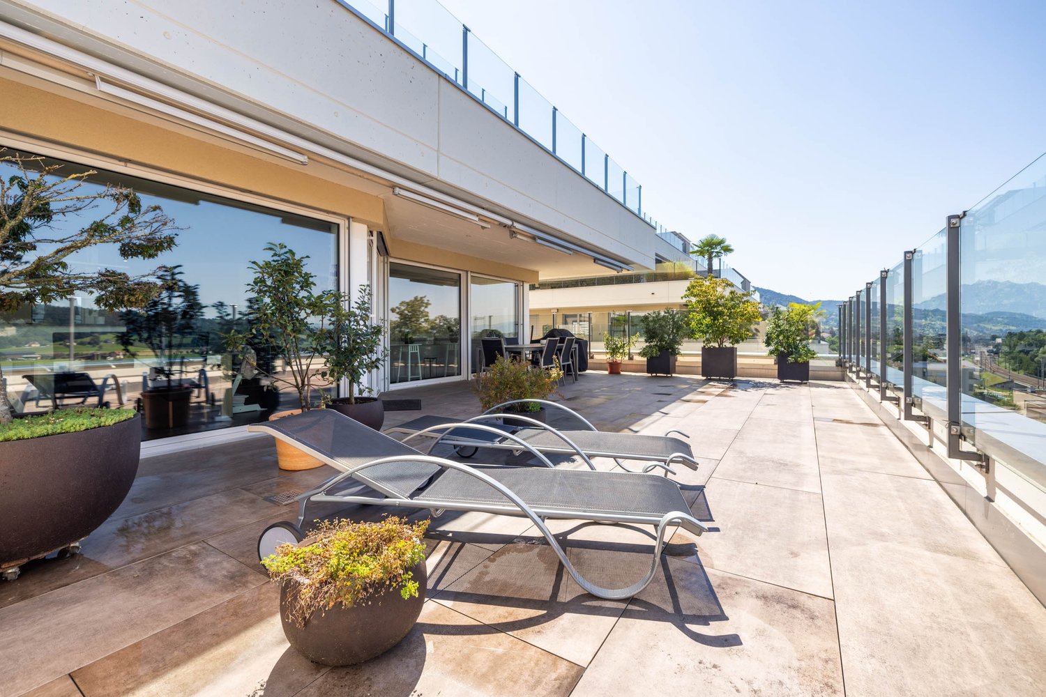 large balcony with lounge chairs, tile flooring, glass railings, multiple potted plants, and a distant mountain view