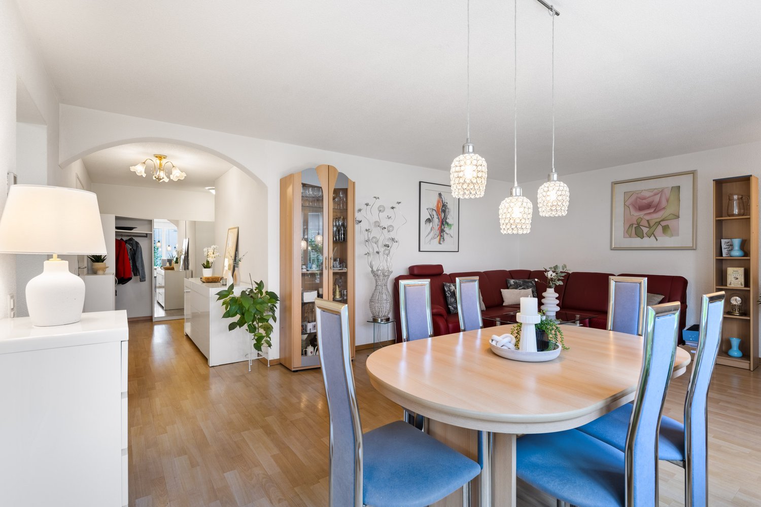 dining room with wood floor, dining table, chairs, lamp, cupboard, plant, artwork, and hallway