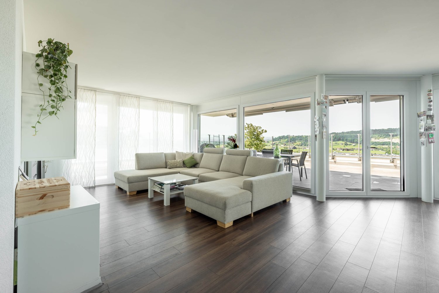 L-shaped couch, coffee table, sliding doors, balcony, wooden floor, white walls, plants