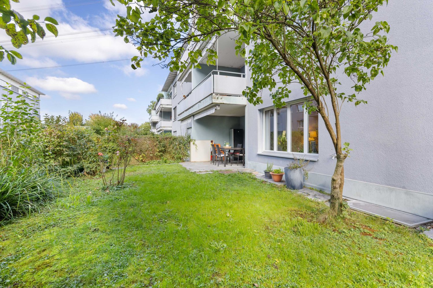 Apartement building with terrace, dining table, well-maintained lawn, tree, potted plants