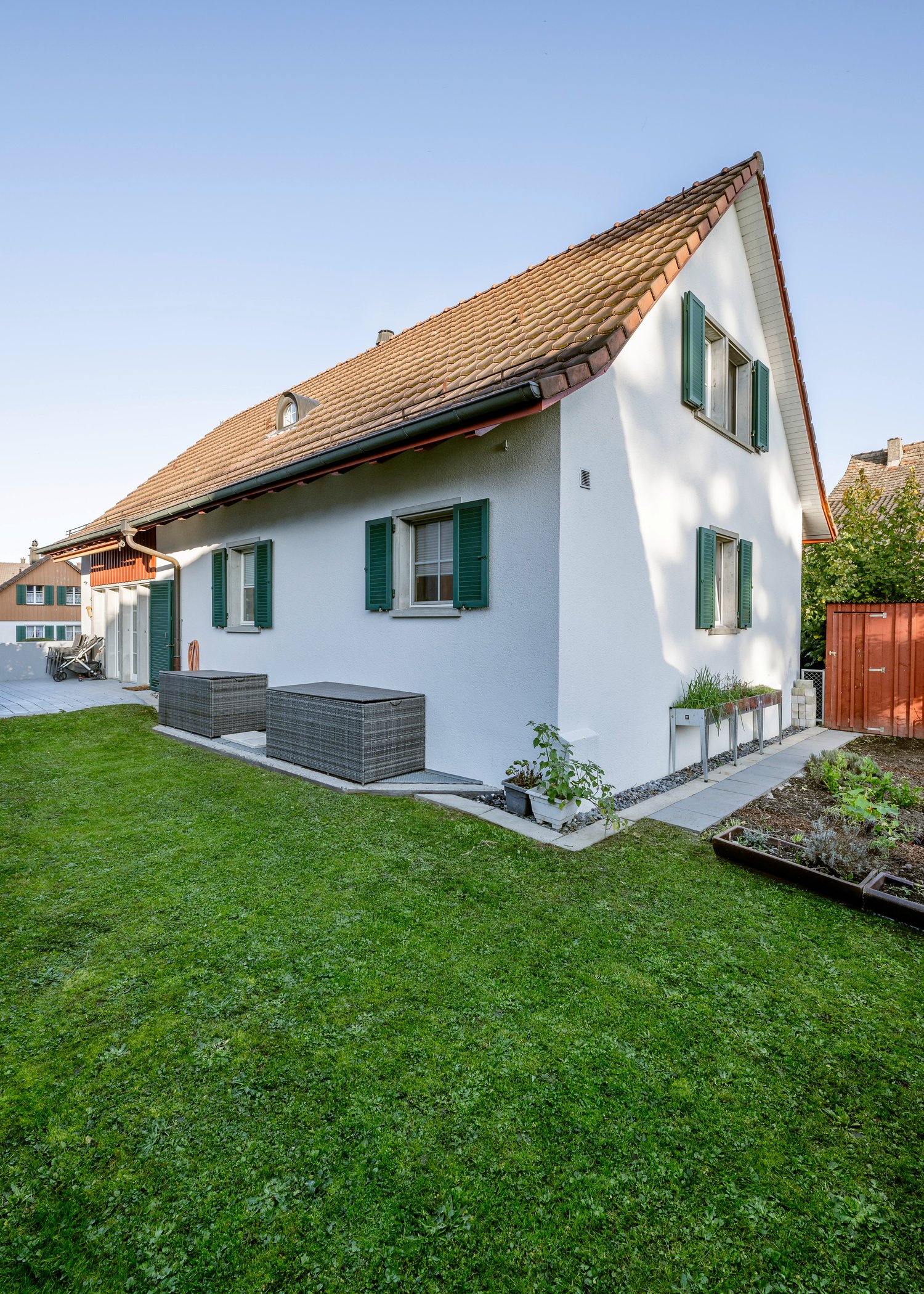 2 story house, white walls, green shutters, red roof, garden, outdoor loungers