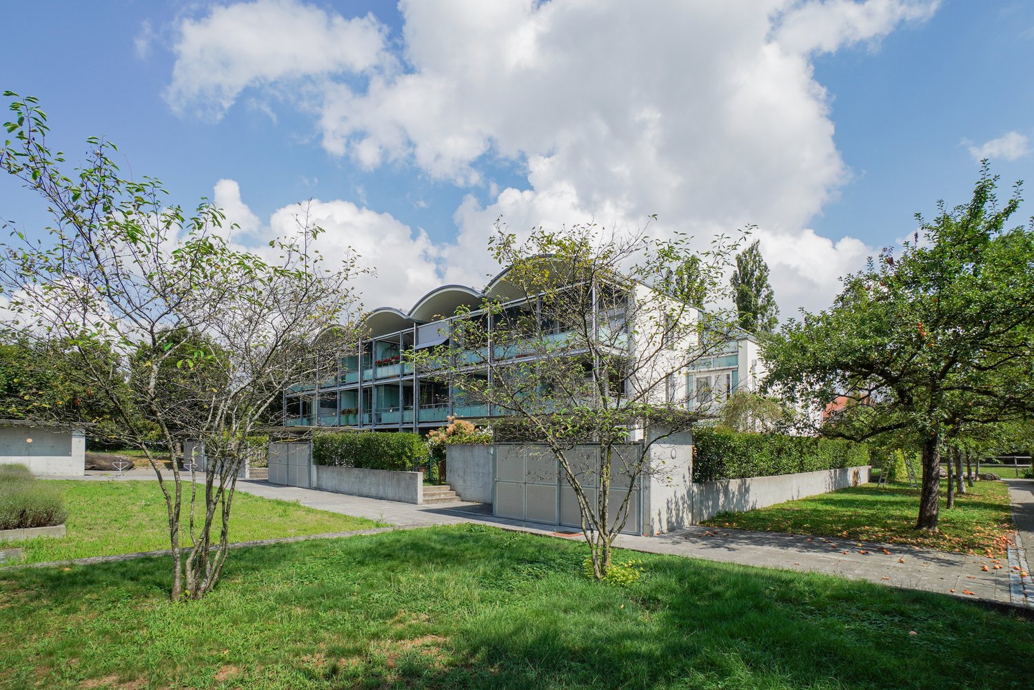 modern apartment building with multiple stories, green balconies, concrete wall, trees, garden