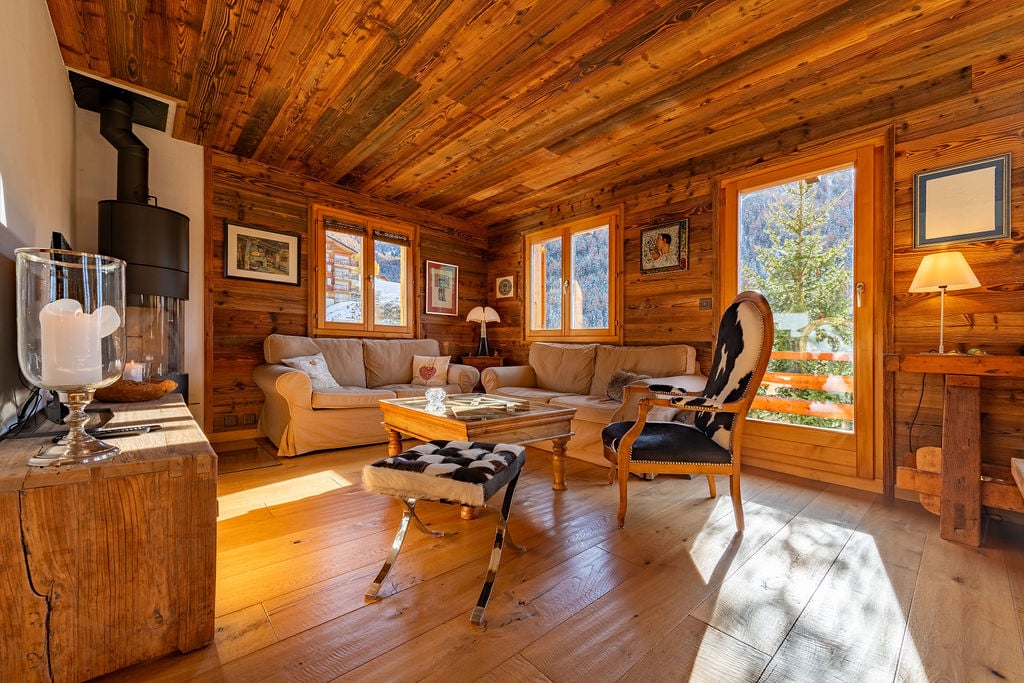 Cozy living room with wooden walls and ceiling, large windows, comfortable sofas, wooden coffee table, and a fireplace