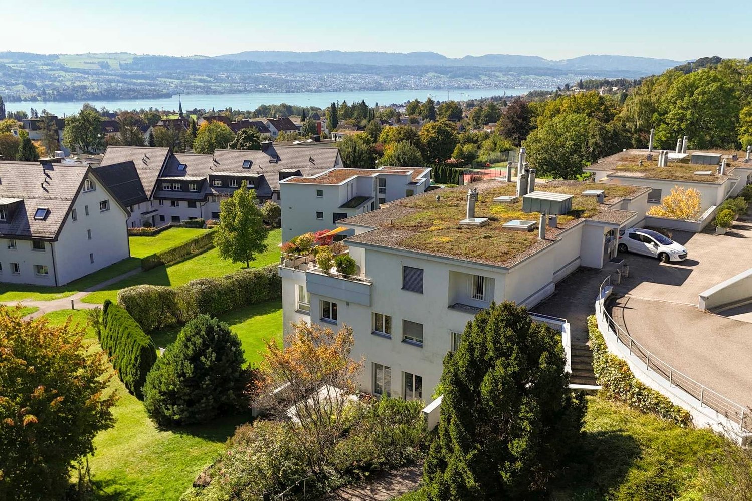 Modern apartment buildings with a green roof, located on a hill with a view of the lake and mountains