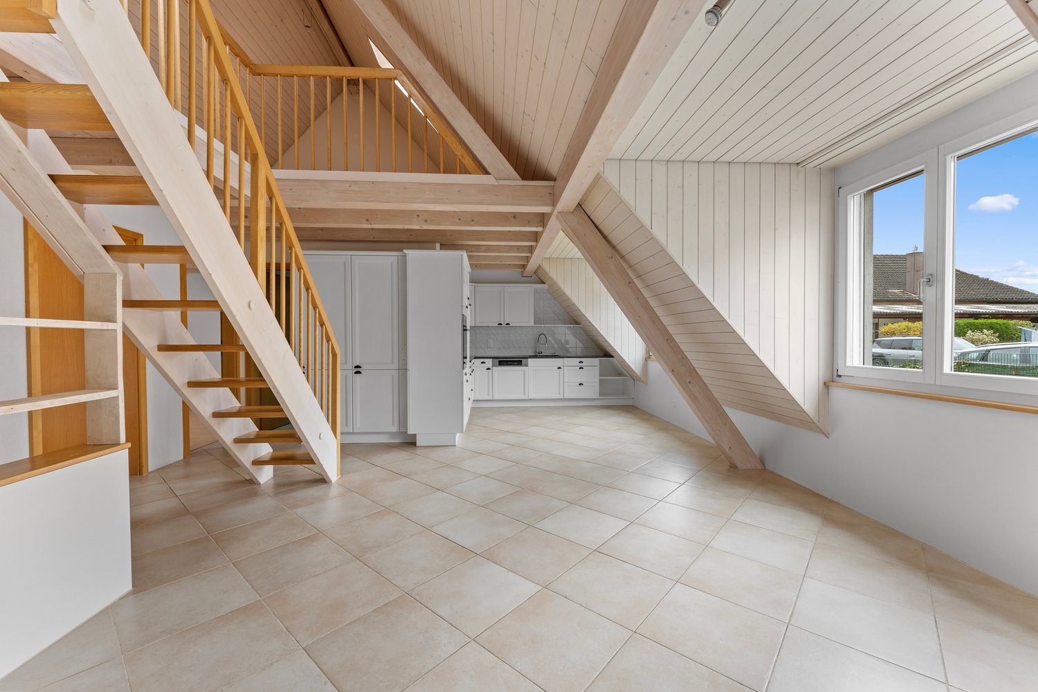 A room with wooden beams, tiled floor, white cabinets, and a staircase.