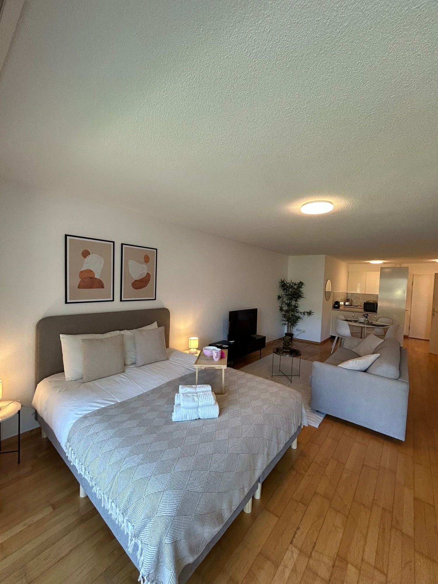 a bedroom with a large bed, two nightstands, a couch, a television, a microwave, a desk, and a dining table with chairs