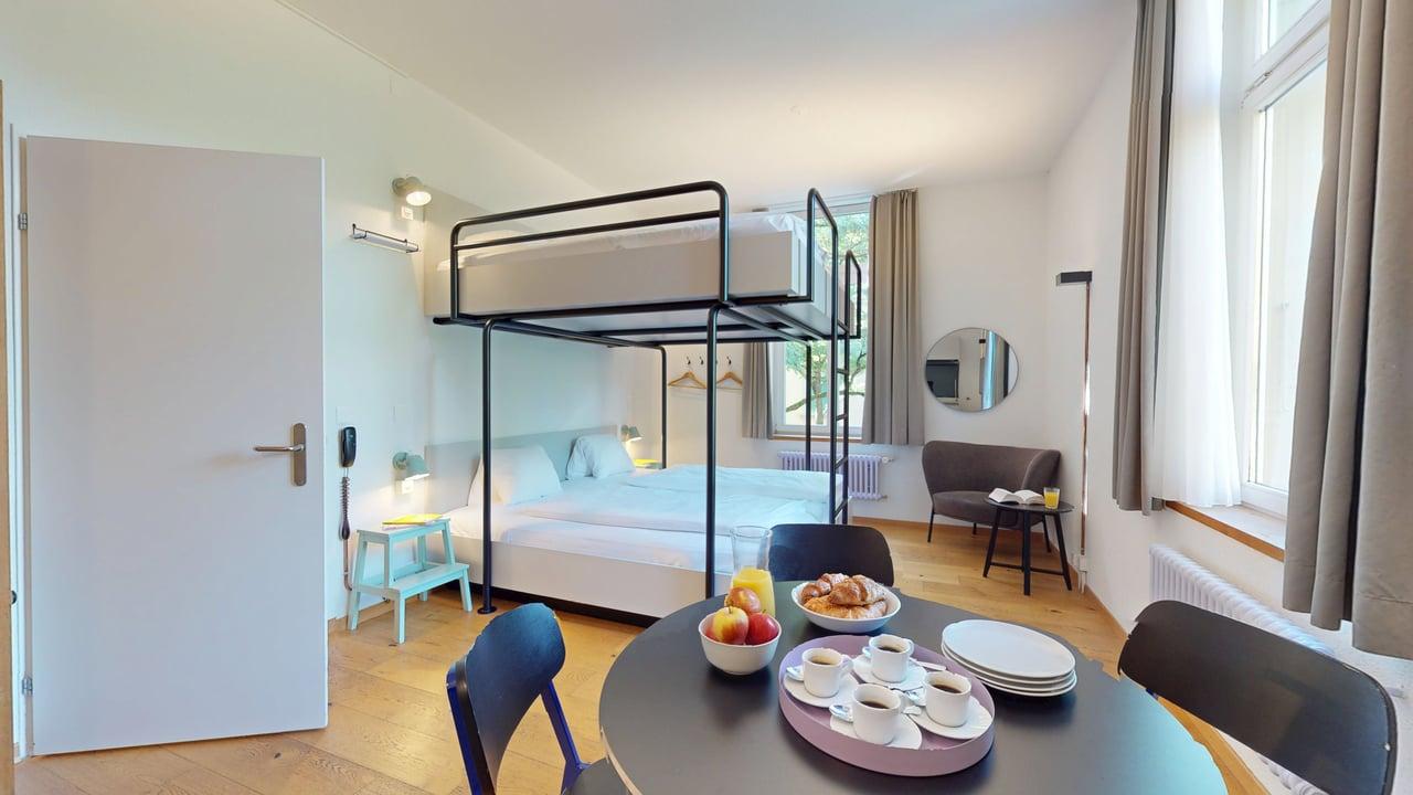 wooden floor, white door, bunk bed, table with breakfast, chair, mirror, window, radiator