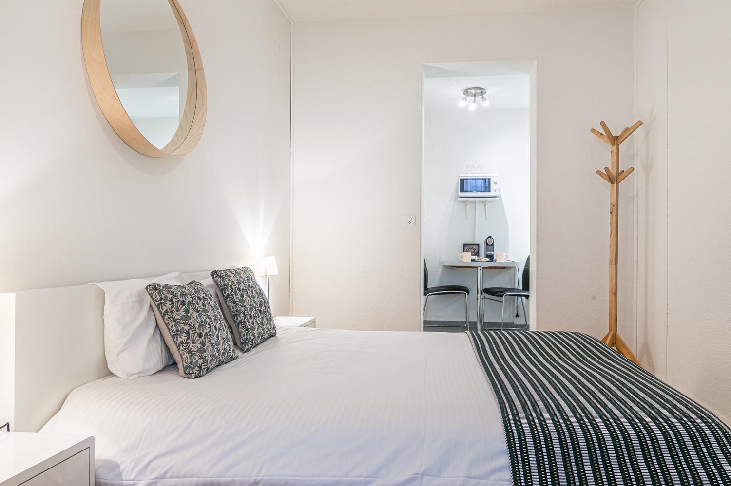 double bed, lamps, mirror, coat rack, microwave, coffee table with chairs, white walls