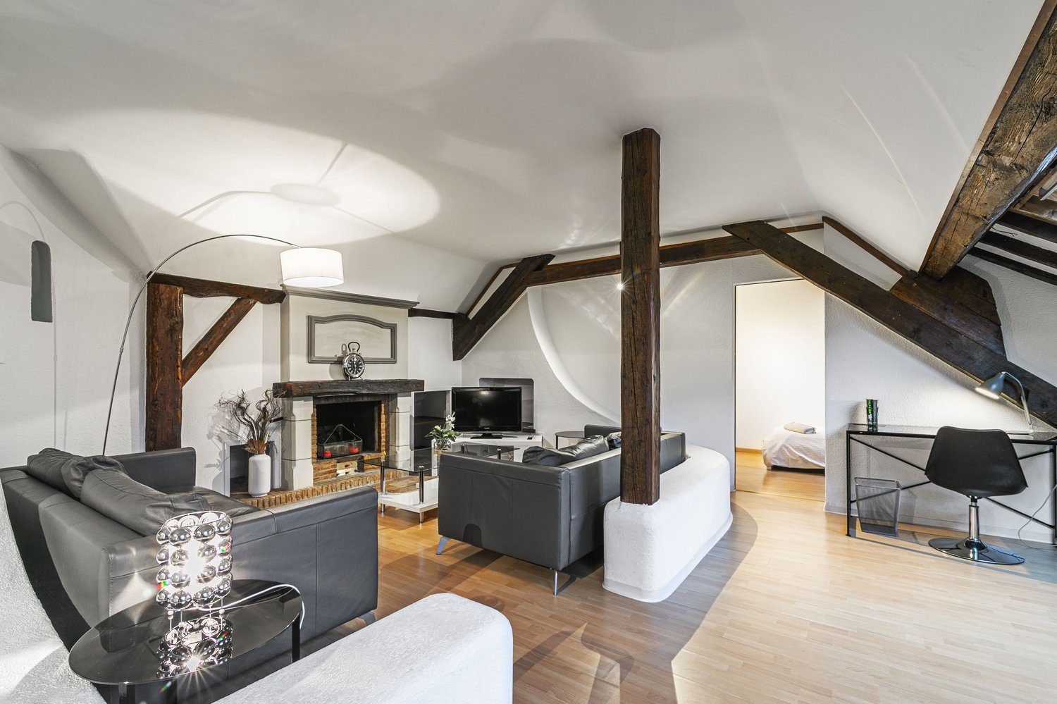 open living room with exposed beams, fireplace, modern furniture, wooden floor, white walls, TV, and decorative items