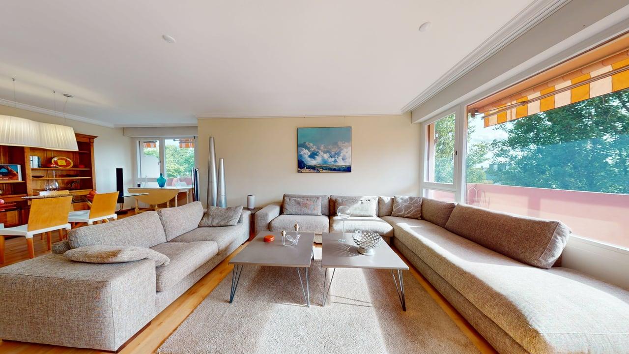 open plan living and dining area, wooden floor, large windows, beige sectional sofa, coffee tables, beige rug, chandelier, framed painting, buffet, dining table and chairs