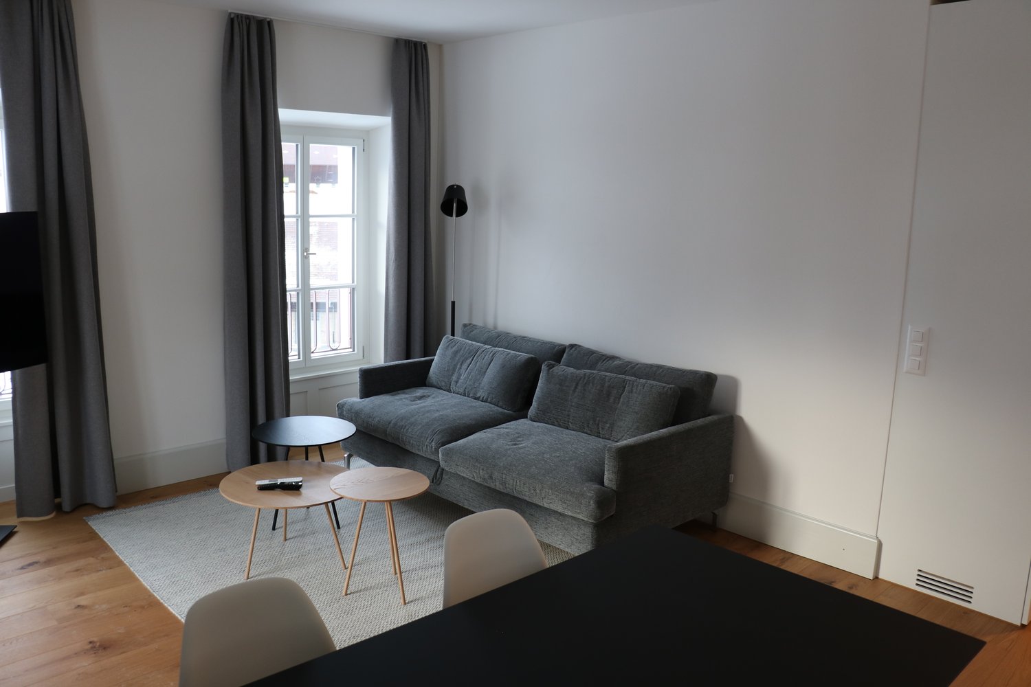 Living room with couch, side tables, chairs, carpet, window, curtains, remote controls