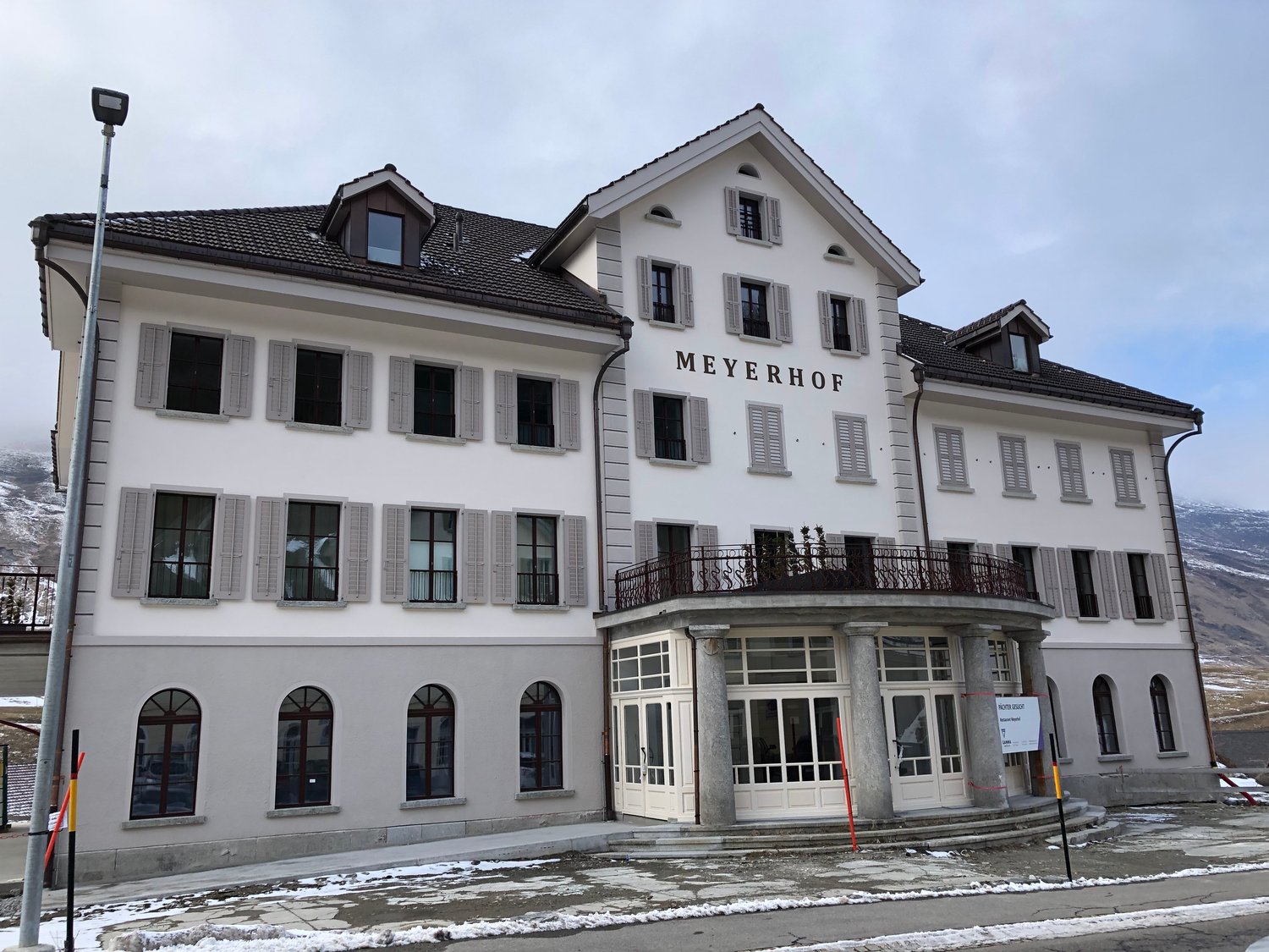 large white building, 'Meyerhof' text on front, large balcony with railing, many windows, white exterior, grey shutters, large arched windows on ground floor